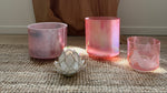 Three pink Alchemy Crystal bowls on a textured surface with a curtain and window in the background.
