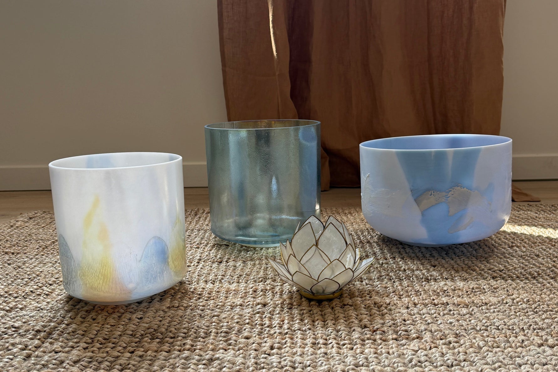 Three Alchemy Crystal Bowls in blue shades on a textured rug with a curtain in the background