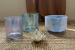 Three Alchemy Crystal Bowls and a decorative candle holder on a textured surface with a curtain in the background.