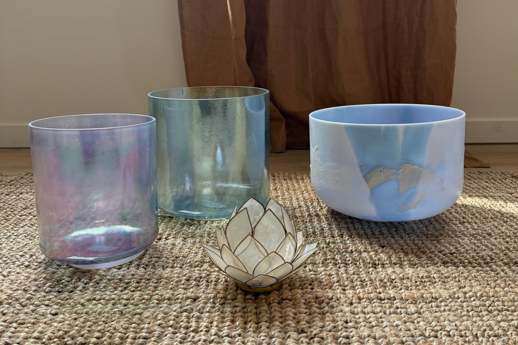 Three Alchemy Crystal Bowls and a decorative candle holder on a textured surface with a curtain in the background.